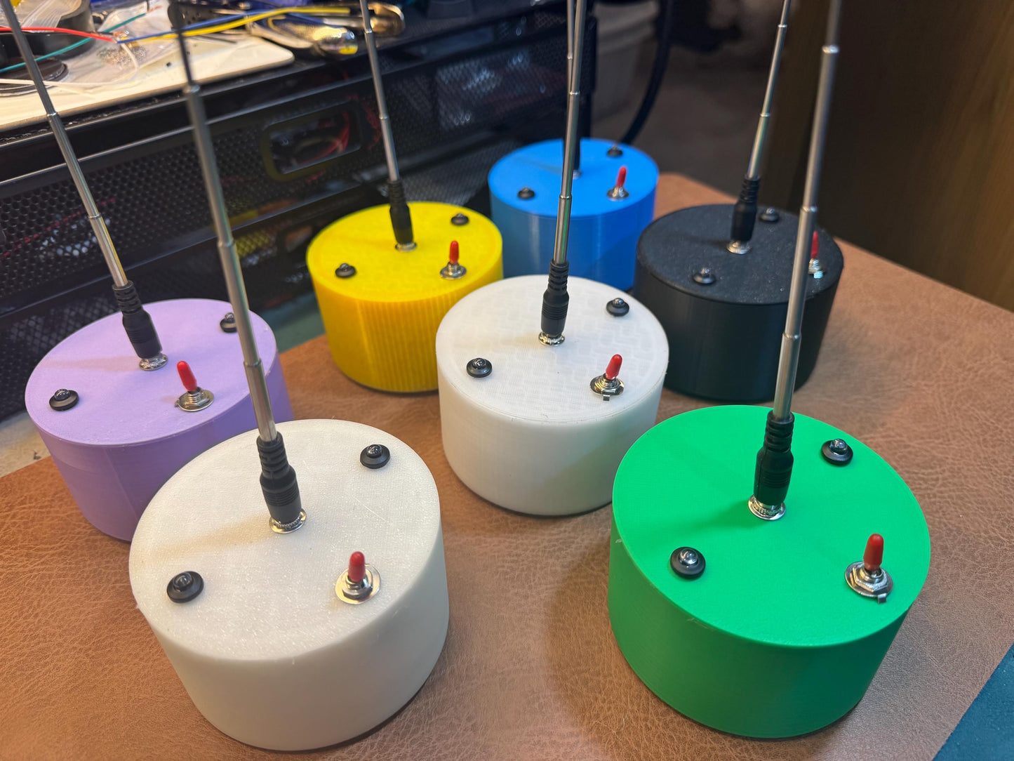 May include: Six small, round, colorful devices with antennas. The devices are white, purple, yellow, blue, black, and green. Each device has a small red button on the top.