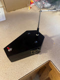 May include: A black coffin-shaped box with a silver antenna extending from the top. The box has a small red switch on the side and a gold latch on the front.