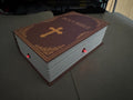 May include: A closed book with a brown leather cover and gold lettering that reads 'HOLY BIBLE'. The book has a cross design on the front cover. There are two red LED lights on the bottom edge of the book.