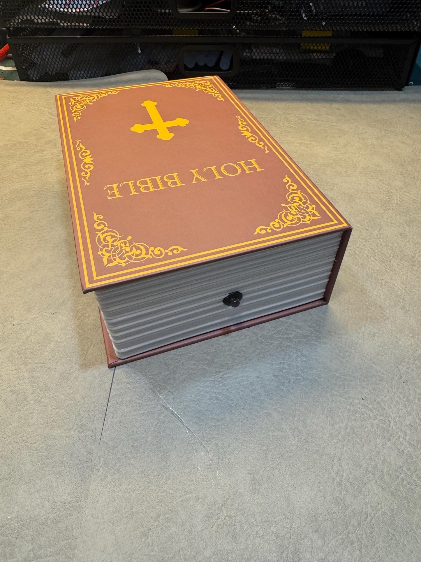 May include: A closed book shaped like a bible with a gold cross on the front cover. The cover is brown with gold trim and the words 'HOLY BIBLE' are printed in gold letters.