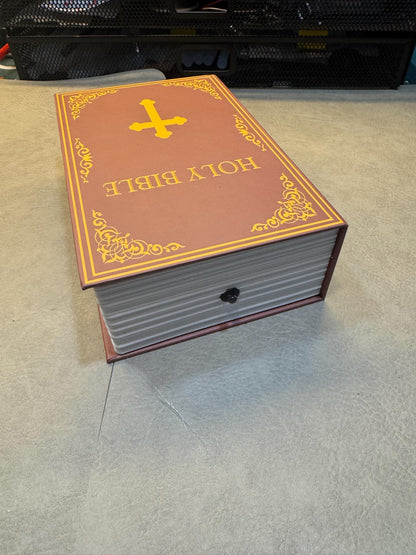 May include: A closed book shaped like a bible with a gold cross on the front cover. The cover is brown with gold trim and the words 'HOLY BIBLE' are printed in gold letters.