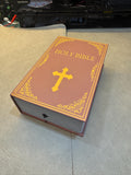 May include: A closed book with a brown cover and gold lettering that reads 'HOLY BIBLE' with a gold cross on the front.