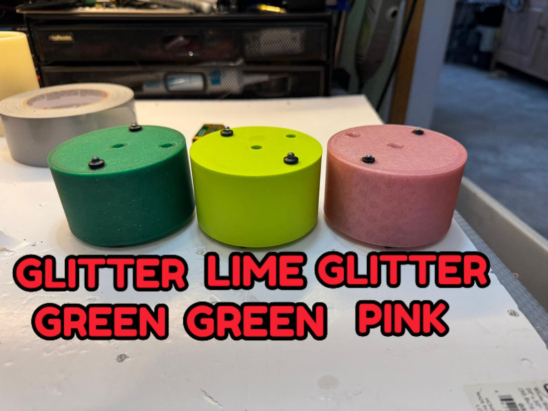 May include: Six small, round, colorful devices with antennas and red buttons. The devices are arranged in a circle on a brown surface. The devices are white, green, black, blue, yellow, and purple.